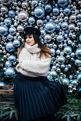  young woman in warm oversize sweater posing near christmas decorations outdoor