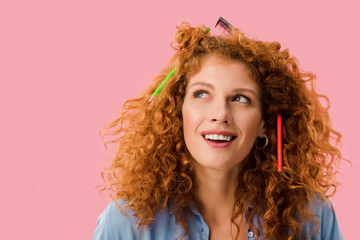 redhead woman with pencils in hair isolated on pink
