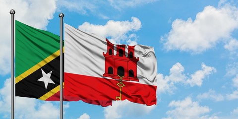 Saint Kitts And Nevis and Gibraltar flag waving in the wind against white cloudy blue sky together. Diplomacy concept, international relations.