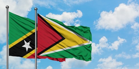 Saint Kitts And Nevis and Guyana flag waving in the wind against white cloudy blue sky together. Diplomacy concept, international relations.
