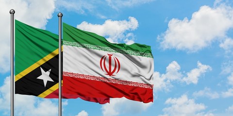 Saint Kitts And Nevis and Iran flag waving in the wind against white cloudy blue sky together. Diplomacy concept, international relations.