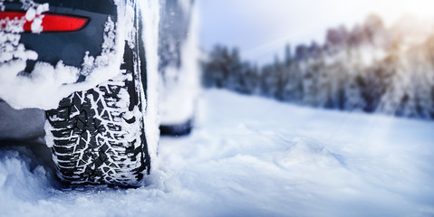 Winter tire detail in snowy mauntains. Car tires in snow with sun lights in background.