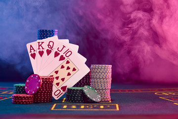 Winning combination in poker leaning on colored chips piles on blue cover of playing table. Black, smoke background, red and blue backlights. Casino. - obrazy, fototapety, plakaty
