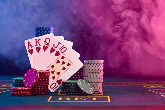 Winning combination in poker leaning on colored chips piles on blue cover of playing table. Black, smoke background, red and blue backlights. Casino.