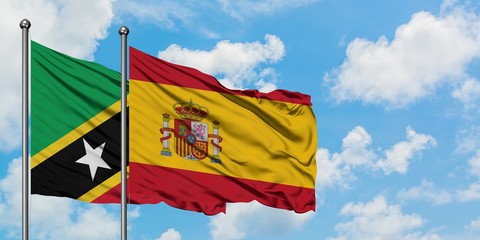 Saint Kitts And Nevis and Spain flag waving in the wind against white cloudy blue sky together. Diplomacy concept, international relations.