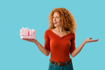 attractive redhead woman holding pink gifts isolated on blue