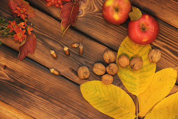 Autumn composition on a wooden background. Apples, nuts, leaves and flowers.