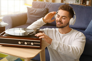 Young man listening to music through record player at home © Pixel-Shot