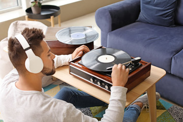 Young man listening to music through record player at home