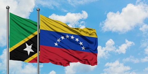 Saint Kitts And Nevis and Venezuela flag waving in the wind against white cloudy blue sky together. Diplomacy concept, international relations.
