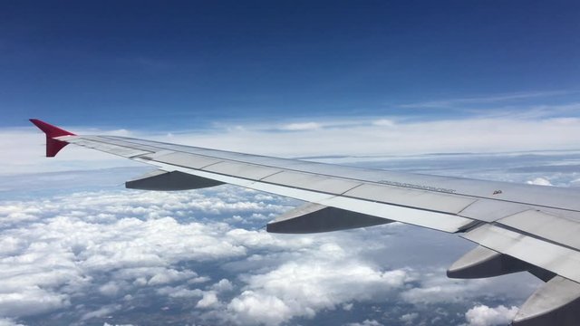 Airplane flight. Wing of an airplane flying above the beautiful clouds and blue and white clean sky. View from the window of the plane. Aircraft. Traveling by air. 4K UHD video. Traveling concept