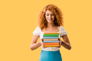 beautiful redhead student holding books isolated on yellow