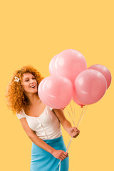 happy young redhead woman with pink balloons isolated on yellow