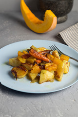 Warm autumn salad with pumpkin, potatoes, carrots on a platter on a gray concrete background.
