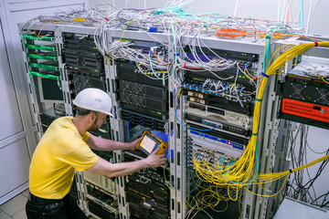 The engineer in a white helmet measures the level of the optical signal in the server room of the data center. A technician diagnoses a problem area in a telecommunication network.