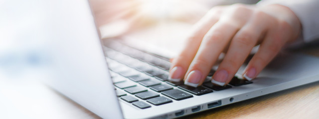 Business woman working on modern computer banner or panorama. Person buying online at internet. Laptop focused on keyboard detail with blur hand. copy space for text.