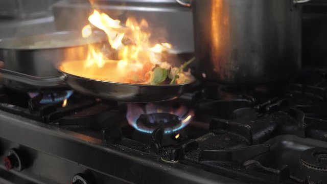 Slow motion closeup of a chef preparing flambe style dish on a frying pan.