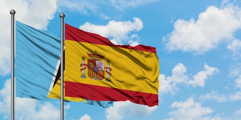 Saint Lucia and Spain flag waving in the wind against white cloudy blue sky together. Diplomacy concept, international relations.