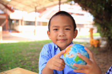 An Asian boy is pointing at the globe in his hand.