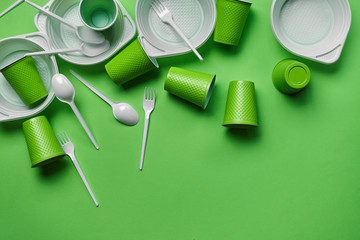 White plastic disposable tableware on green background with copy space. The concept of picnic...