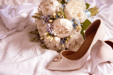 wedding bouquet of white peonies and blue flowers, white stiletto pumps with  rings on a white sheet