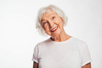 Lovely, cheerful and positive old woman on picture. Smile and look up. Dreaming about something. Wear white shirt. Elder with gray hair on picture. Isolated over white background.