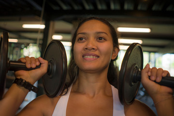 fitness club lifestyle portrait of young attractive and happy athletic Asian Indonesian woman training hard at gym lifting weight dumbbells sweaty and cheerful in sport concept