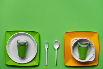 Colorful plastic disposable tableware on green background with copy space. The concept of picnic utensil. Top view. Selective focus. Close-up.