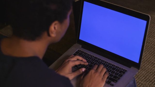 Dark skinned man types on blue screen computer close up