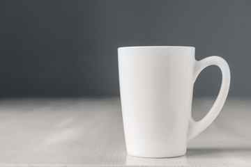 White ceramic cup on white wooden table on gray background. Place for text or advertising