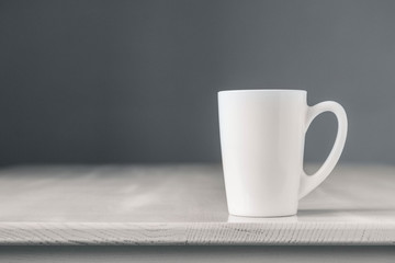 White ceramic cup on white wooden table on gray background. Place for text or advertising