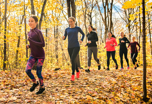 woman group out running together in an autumn park they run a race or train in a healthy outdoors lifestyle concept