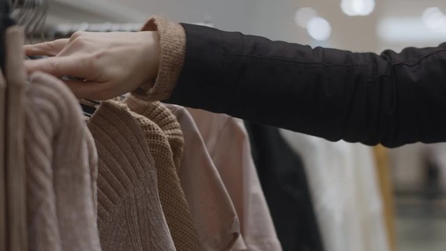 CLOSE UP of a woman going through clothes on a rack in a clothes store.