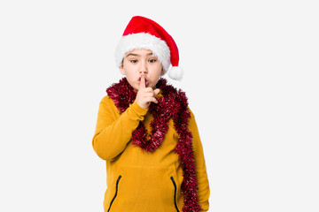 Little boy celebrating christmas day wearing a santa hat isolated keeping a secret or asking for silence.