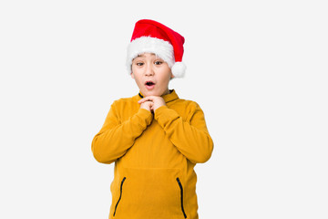 Little boy celebrating christmas day wearing a santa hat isolated praying for luck, amazed and opening mouth looking to front.