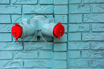 Bright red caps on a wall mounted fire hydrant contrast with a painted turquoise brick wall.  