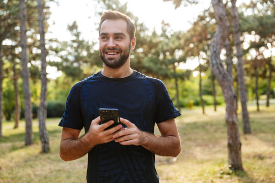 Photo of young smiling man using cellphone while working out