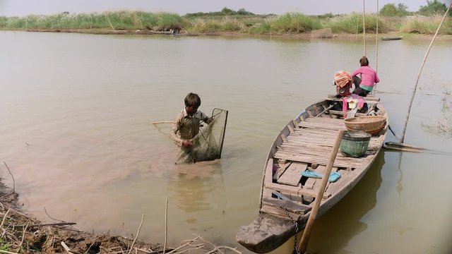 Clammer pouring clams into a bamboo basket held by his wife sitting in a dugout canoe