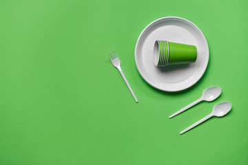 Colorful plastic disposable tableware on green background with copy space. The concept of picnic utensil. Top view. Selective focus. Close-up.