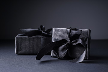 Black friday concept. Gifts in black packaging with black ribbons on a black and gray background.
