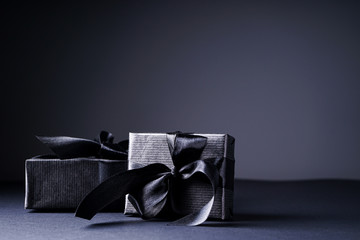 Black Friday concept. Gifts in black packaging with black ribbons on a black and gray background. Copy space.