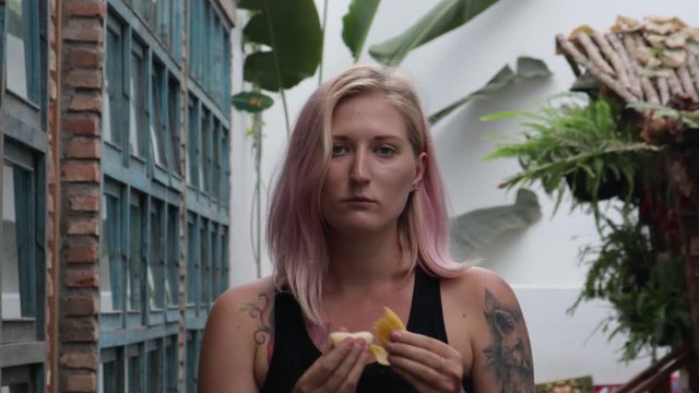 Satisfied girl with tattoos eats fruit.