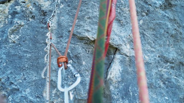 First person view of male hand reaching hold on a vertical cliff. person hanging on a ascender device attached to rope, several ropes on which a person hangs.