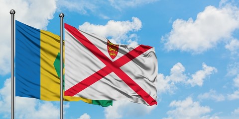 Saint Vincent And The Grenadines and Jersey flag waving in the wind against white cloudy blue sky...