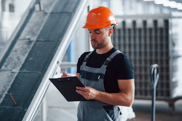 Concentrated at work. Employee indoors in factory. Young technician with orange hard hat