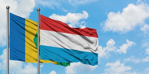 Saint Vincent And The Grenadines and Luxembourg flag waving in the wind against white cloudy blue...