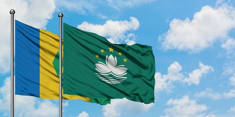 Saint Vincent And The Grenadines and Macao flag waving in the wind against white cloudy blue sky...