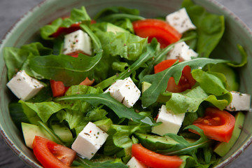 fresh vegetable salad from lettuce, arugula, tomatoes, cucumbers, avocados, feta cheese. On a gray background