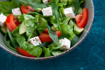 fresh salad in a plate: lettuce, cucumber, avocado, tomato, feta cheese, arugula, spices and herbs. Healthy food. top view