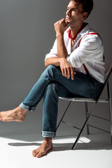 pensive man in white shirt sitting on chair on grey